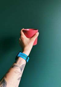 Cropped hand of woman holding container against blue background