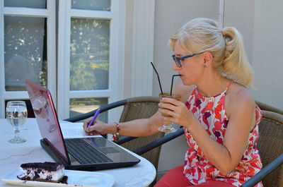 Woman working with technology outside an office and drinking coffee