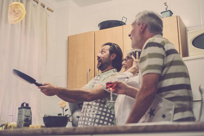 Mature son throwing omelette in pan while happy parents looking in kitchen