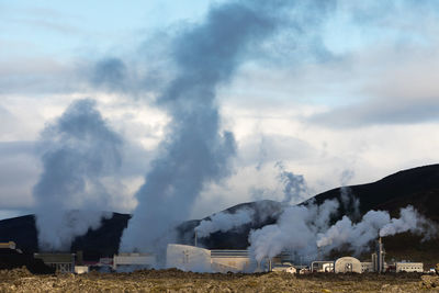 Smoke emitting from chimney on landscape against sky