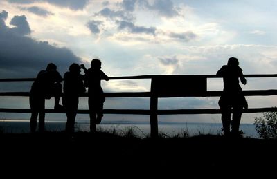 Silhouette men standing by railing against sky during sunset