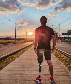 Rear view of man running on railroad track against sky during sunset