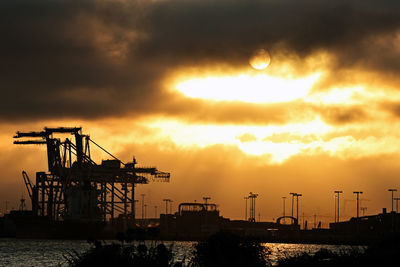 Silhouette cranes by sea against sky during sunset