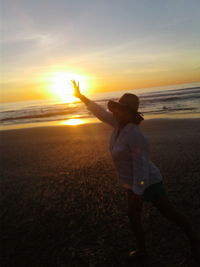 Woman standing on beach against sky during sunset