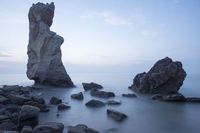 Low angle view of stack rocks in sea against sky at dusk