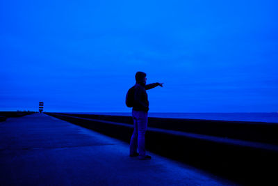 Man pointing at blue sky while standing on promenade at dusk