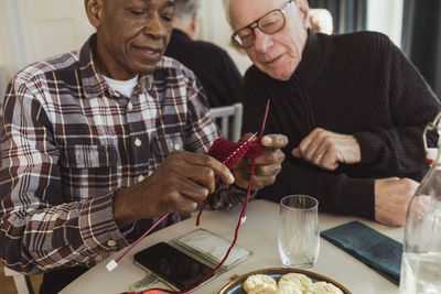 Elderly man knitting by male friend at retirement home