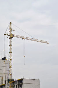 Low angle view of crane at construction site against sky