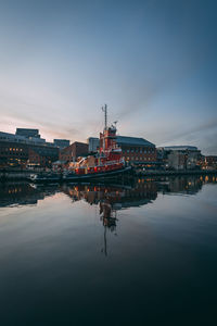 Illuminated buildings by river against sky during sunset