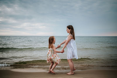 Side view of sisters dancing on beach at lake michigan