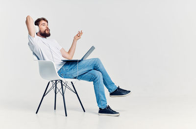 Full length of man sitting on chair against white background