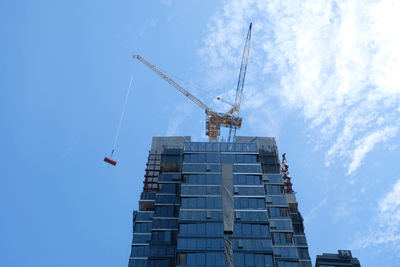 Low angle view of crane by building against sky