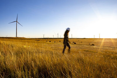 Female operator walks through a wind farm at sunset