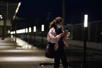 Young woman wearing mask using mobile outdoors