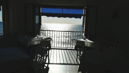 Empty chairs and table in restaurant by sea against sky