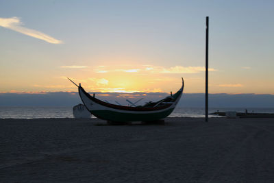 Boat moored on beach against sky during sunset