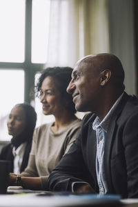 Smiling bald businessman sitting with female colleagues during meeting in creative office