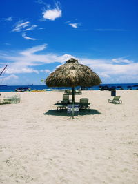 Thatched parasol by deck chairs on sand at beach against sky