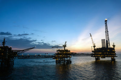 Cranes at commercial dock against sky during sunset