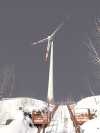 Windmills on snow covered field against sky