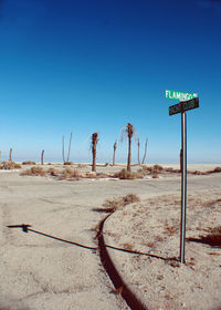 Road sign on desert against clear blue sky