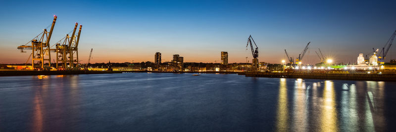 Illuminated commercial dock by city against sky