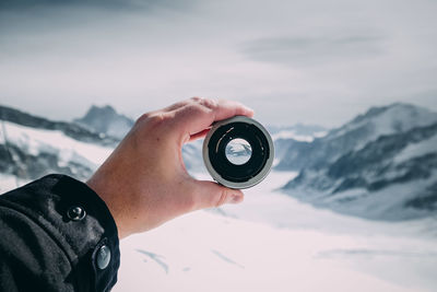 Cropped image of hand holding lens against snowcapped mountains