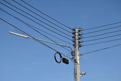 Low angle view of electricity pylon against clear blue sky