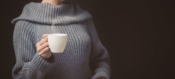 Midsection of woman holding coffee cup against black background