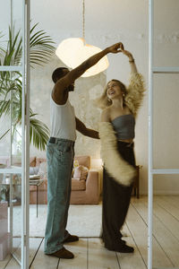 Young man in undershirt holding hands of girlfriend while dancing at home
