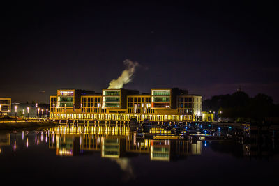 Illuminated factory by lake against sky at night