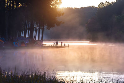 People by lake at forest during foggy weather