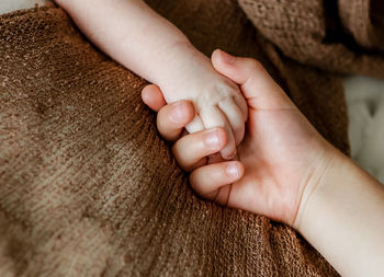 Cropped image of siblings holding hands on bed at home