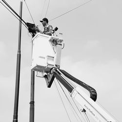 Low angle view of men working on pole against sky
