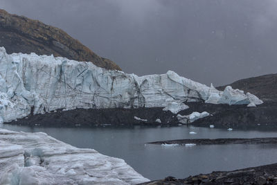 Scenic view of lake by snowcapped mountain against sky