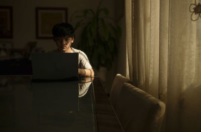 Portrait of teenage asian boy using laptop indoor with sunlight and shadow