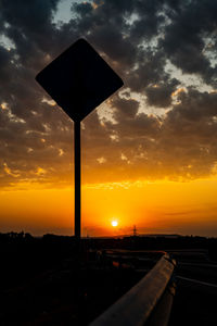 Silhouette road sign against sky during sunset