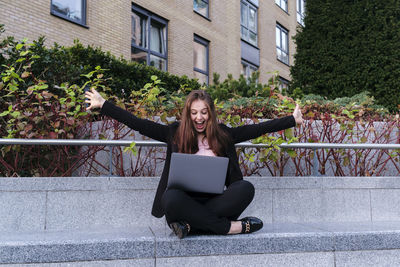 Happy businesswoman with arms outstretched with laptop sitting on bench