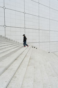 Rear view of man walking on footpath against wall