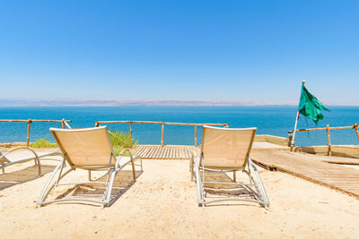 Deck chairs on beach against clear blue sky