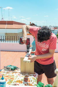 Couple building a piece of furniture on a rooftop on a sunny day.