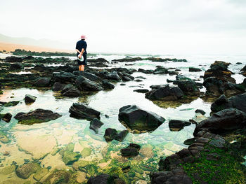 Man standing on rock by sea against sky