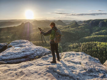 Picture shooting. artist holding camera on tripod and pointing view finder directing into rising sun