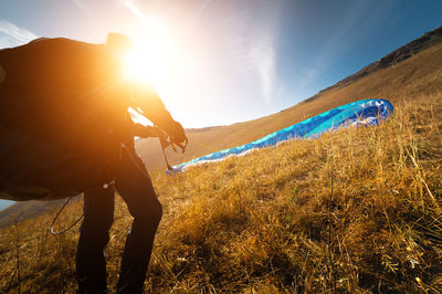 Rear view of woman walking on field against sky during sunset