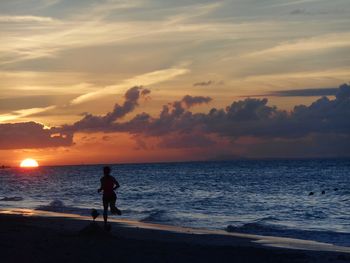Silhouette man standing on beach against sky during sunset