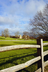 Bare trees on grassy field against cloudy sky