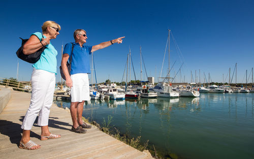 Friends standing on harbor by sea against sky