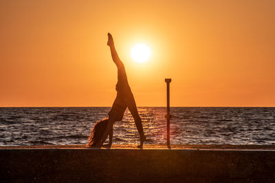 Silhouette woman exercising at beach against sky during sunset