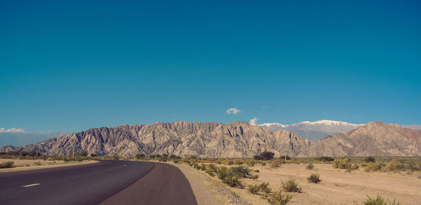 Road amidst desert against clear blue sky