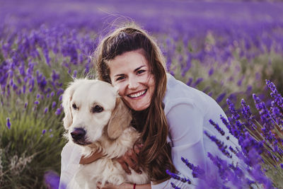 Portrait of cheerful woman with dog by purple flowering plants on land